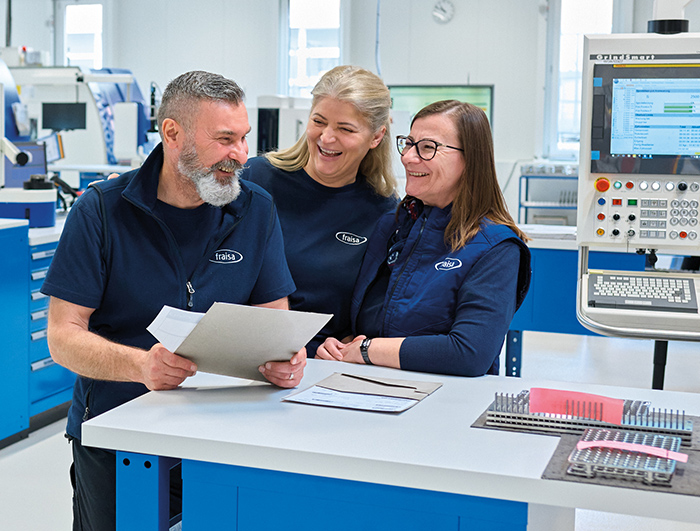 Drei FRAISA Mitarbeiter stehen an einem Tisch und unterhalten sich.